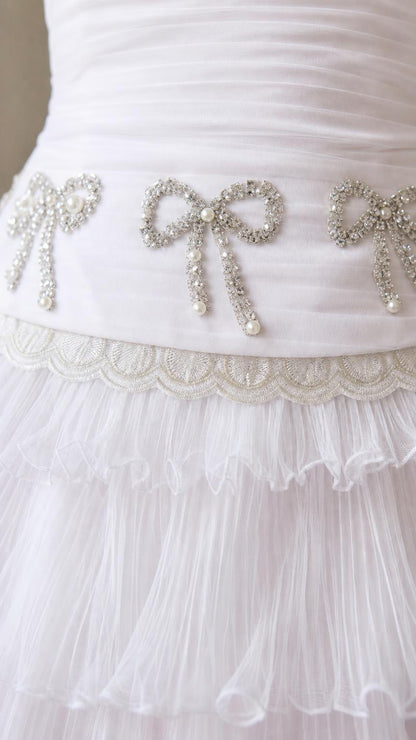 Close-up detail of rhinestone bow waist embellishment on white dress