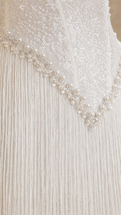 Close-up detail of white sequin bodice, pearl waist trim, and fringe skirt