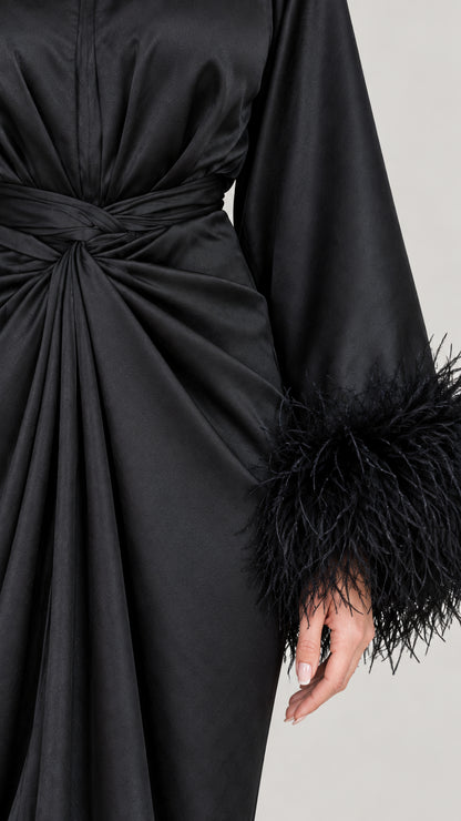 Close-up of twist waist detail and feather-trimmed cuff on black satin dress
