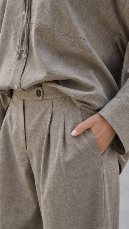 Close-up of pleated waist and side pocket on taupe trousers