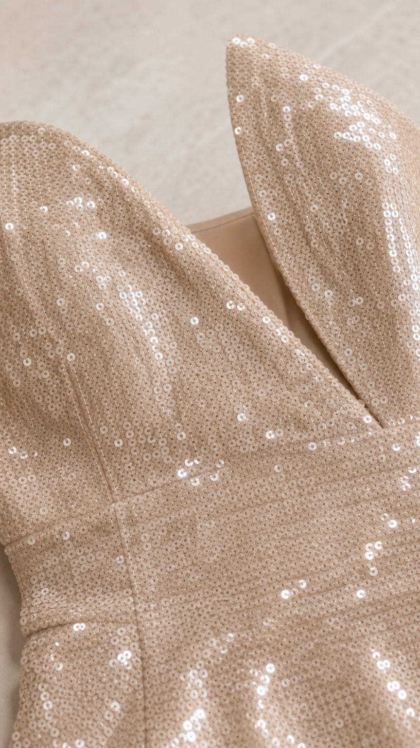 Close-up detail of shimmering champagne sequins and sculptural split neckline