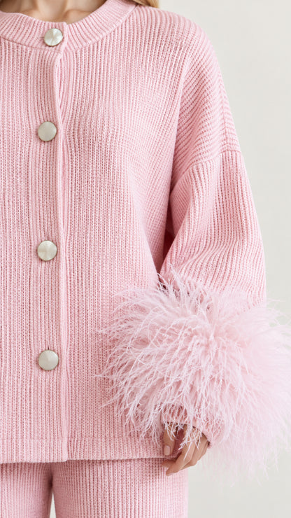 Close-up detail of pink ribbed knit cardigan fabric, buttons, and fluffy feather-trimmed cuffs