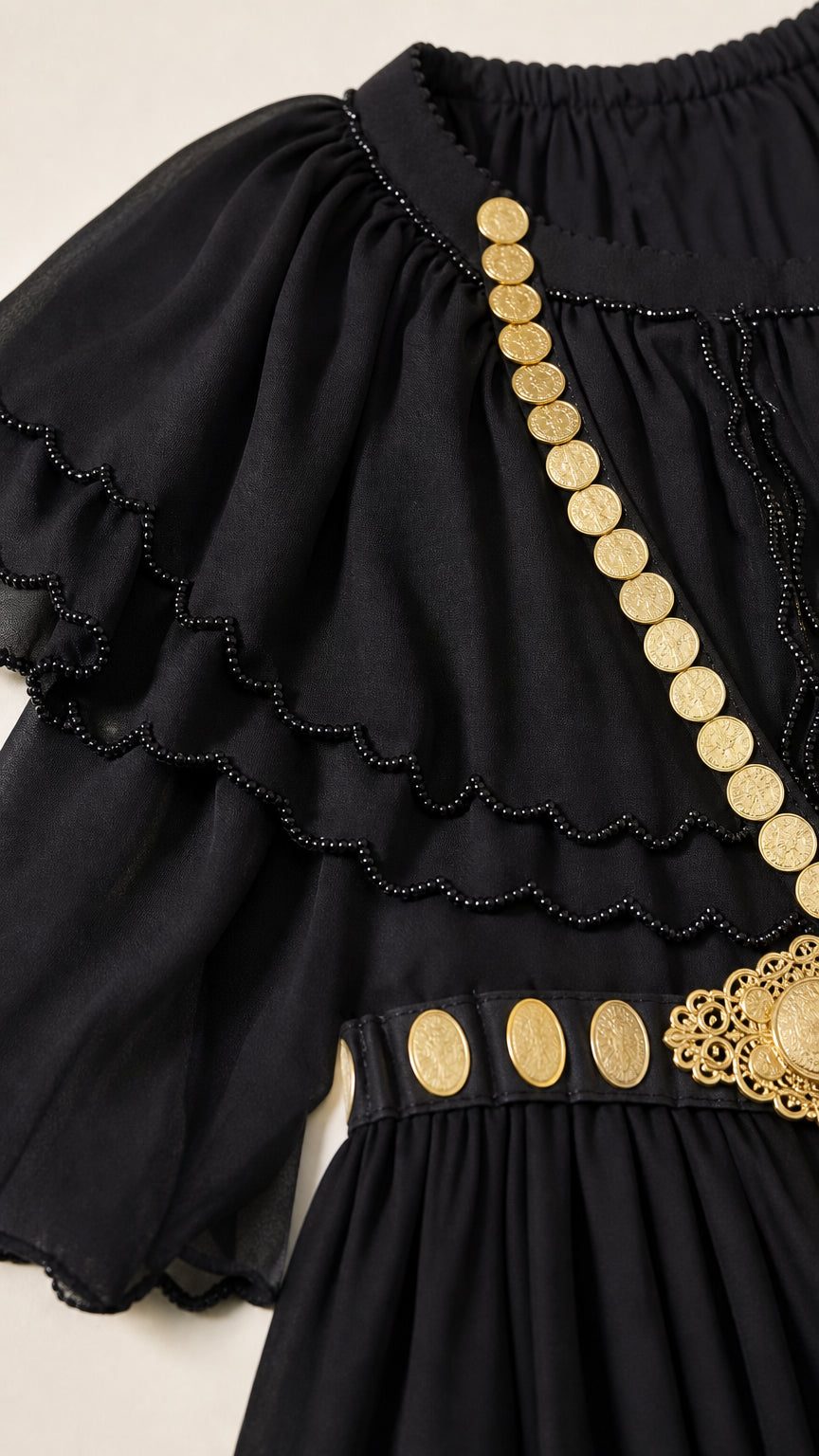 Close-up detail of black scalloped ruffle neckline and gold coin jewelry