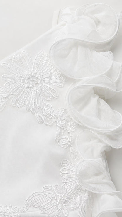 Close-up detail of fabric, ruffles, and floral embroidery