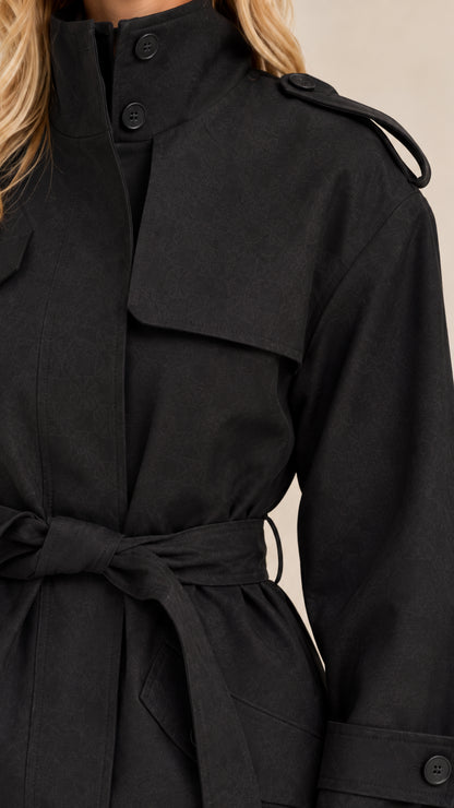 Close-up detail of black short trench coat highlighting stand collar, storm flap, and waist tie