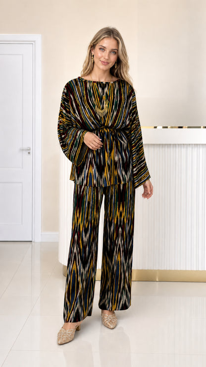 Front full view of woman wearing black and gold ikat print pleated two-piece set