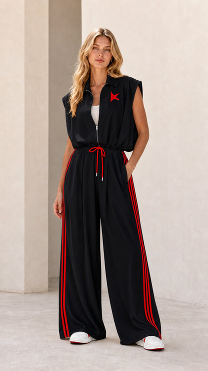 Front view of model wearing black sleeveless wide-leg track jumpsuit with red stripes