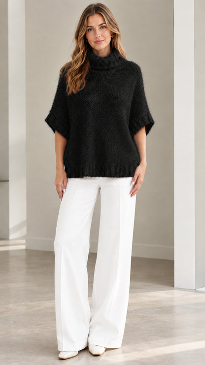 Model wearing Black short sleeve turtleneck poncho knit sweater with white pants
