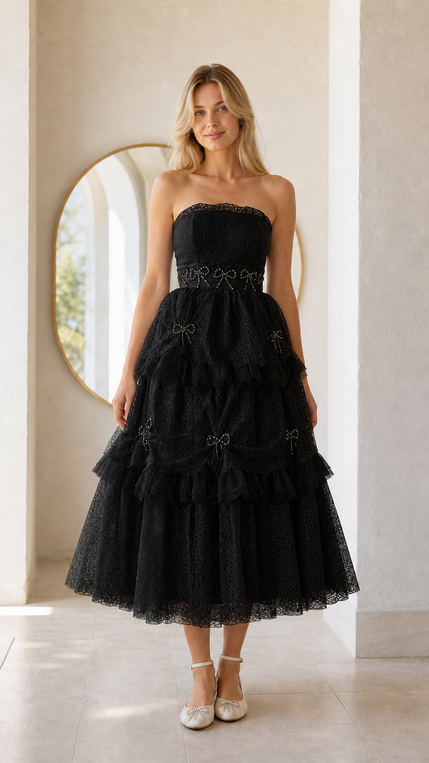 Front full view of woman wearing black strapless tiered midi dress