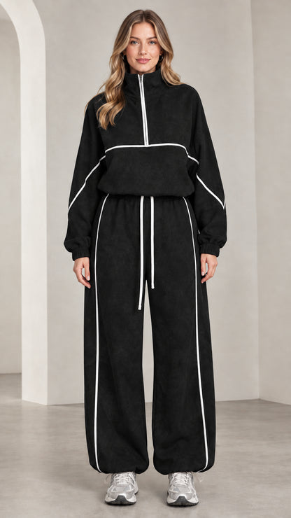 Front view of woman wearing black quarter-zip tracksuit set with white contrast piping