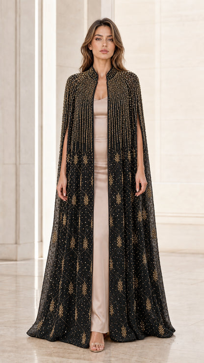 Model wearing black floor-length beaded cape evening gown with gold accents