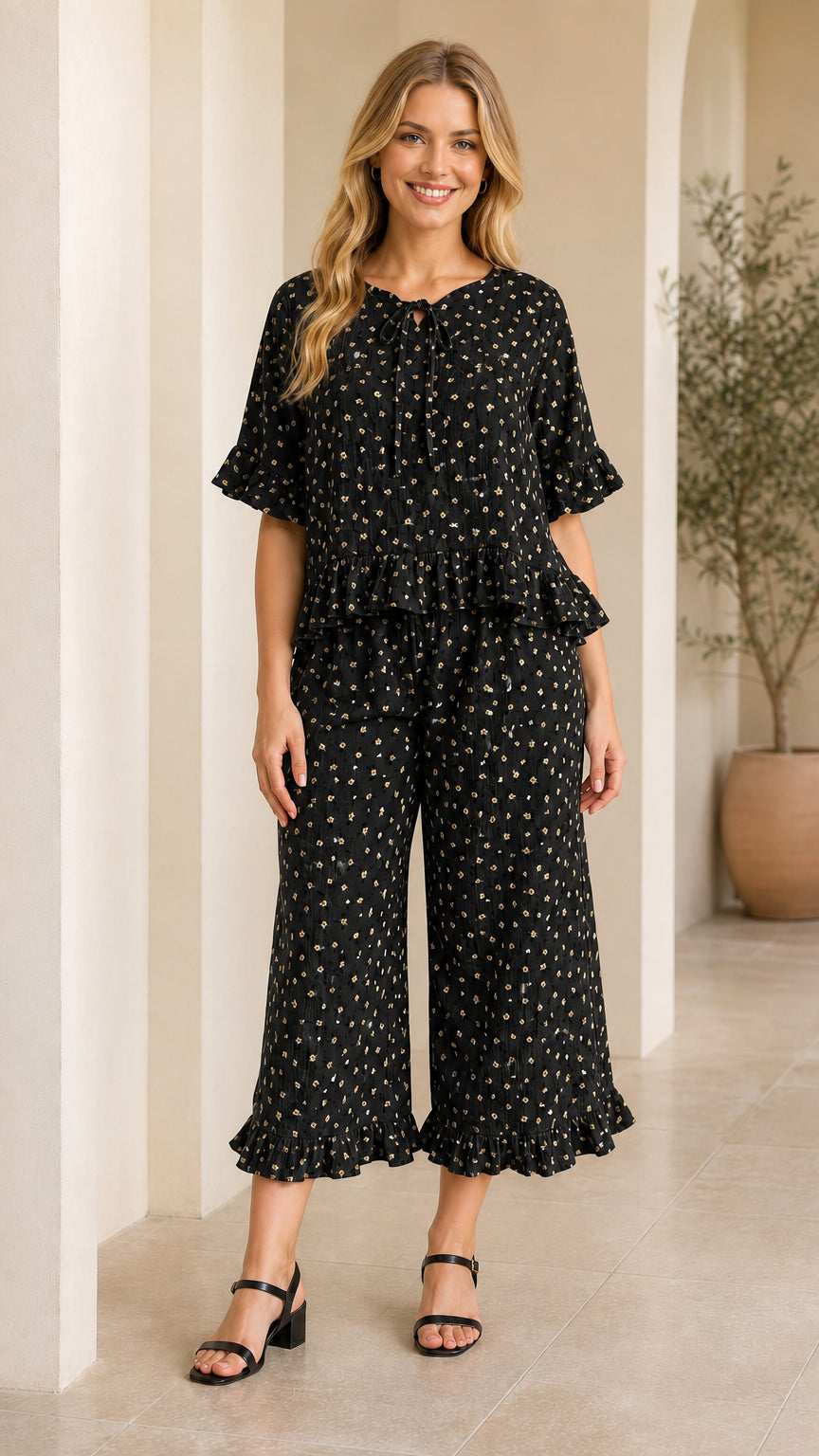 Front view of model wearing black floral tie-neck ruffle top and pants set