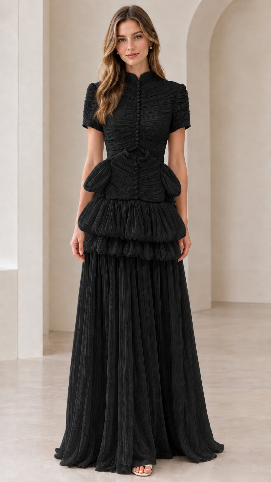 Front view of model wearing black mock neck tiered pleated maxi gown