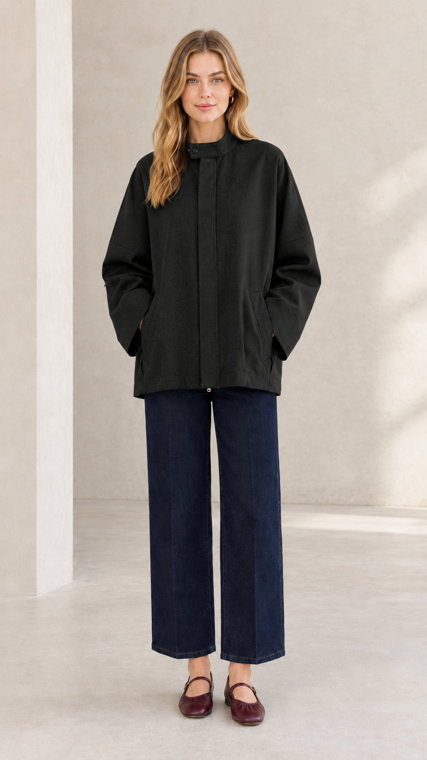 Front view of woman wearing black relaxed stand collar jacket with concealed placket