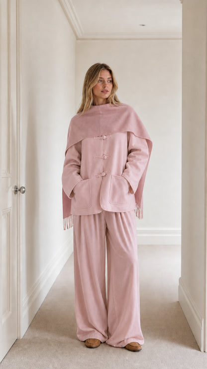 Model wearing dusty pink monochrome toggle button jacket, matching cape, and wide-leg trousers