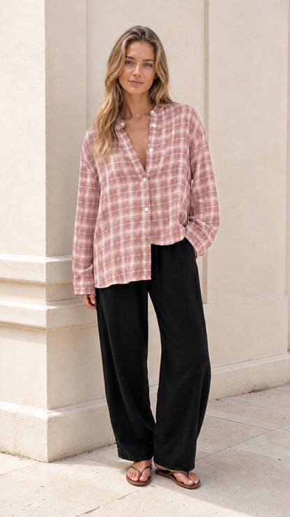 Model wearing dusty pink plaid button-down blouse with black trousers