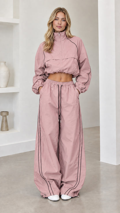 Model wearing dusty pink cropped windbreaker and wide-leg track pants set with dark piping