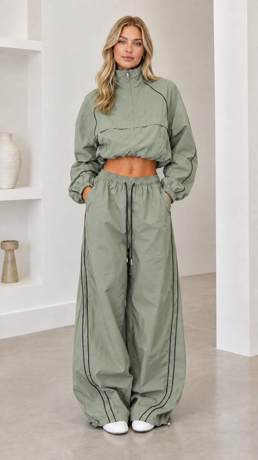 Model wearing sage green cropped windbreaker and wide-leg track pants set with black piping