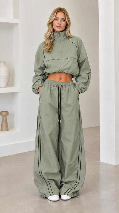 Model wearing sage green cropped windbreaker and wide-leg track pants set with black piping