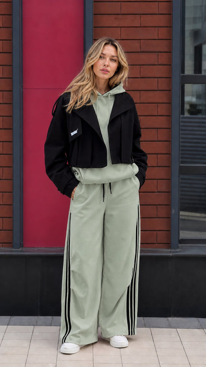 Model wearing sage green hoodie and wide leg pants set with cropped black jacket