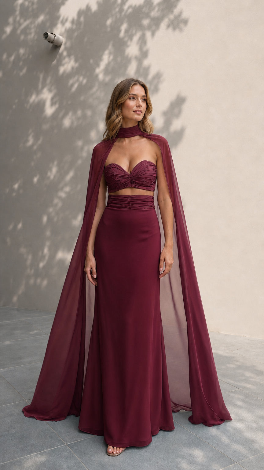 Model in rich burgundy formal two-piece dress with cape