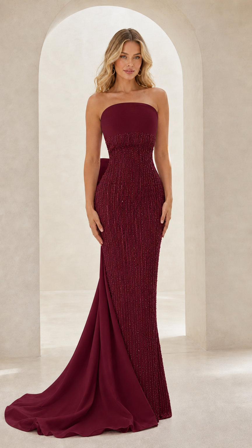Model wearing strapless beaded evening gown with back train in rich burgundy