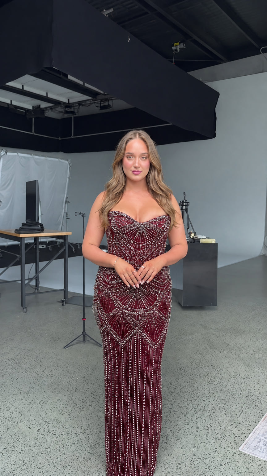 Front view of model wearing strapless beaded burgundy red formal gown