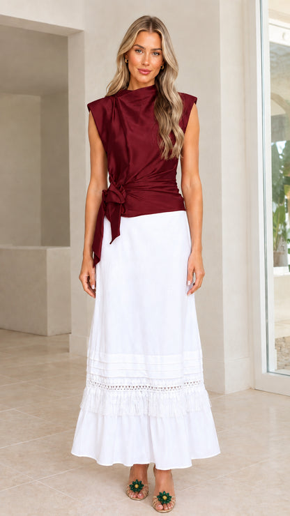 Model wearing burgundy wine sleeveless satin draped top with side tie and white skirt