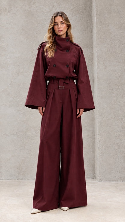 Front full-length view of model in burgundy double-breasted wide-leg trench jumpsuit