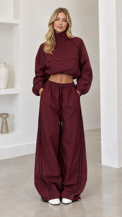 Model wearing burgundy cropped windbreaker and wide-leg track pants set with black piping