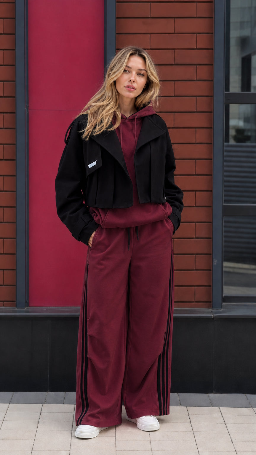 Model wearing burgundy hoodie and wide leg pants set with cropped black jacket