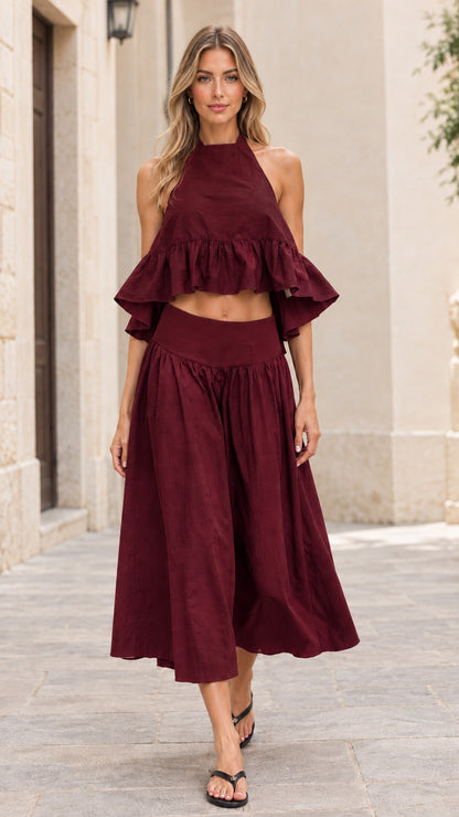 Front full-length view of model wearing burgundy red halter crop top and midi skirt set