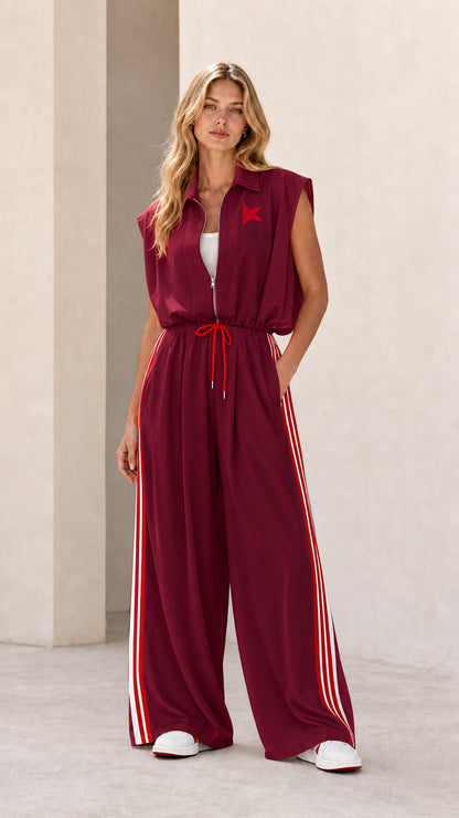 Front view of model wearing burgundy sleeveless wide-leg track jumpsuit with red stripes