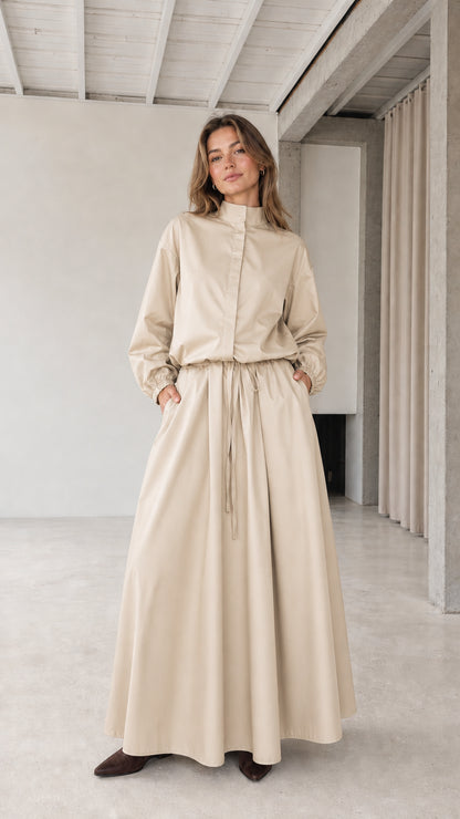 Front full view of woman wearing beige stand collar drawstring maxi dress